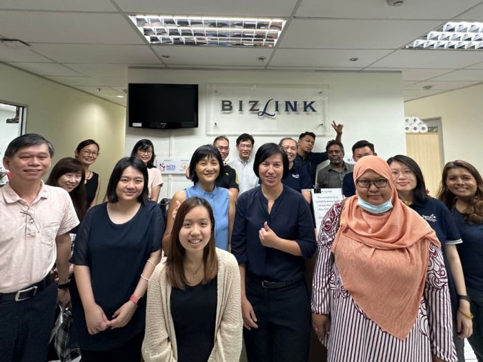 Group photo of guests from SAMH with CEO Li May infront of the Bizlink signboard