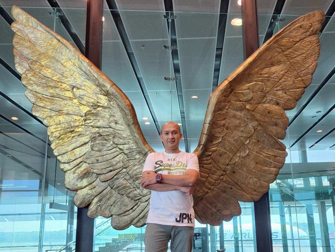 Vincent standing against gold coloured angel wings 